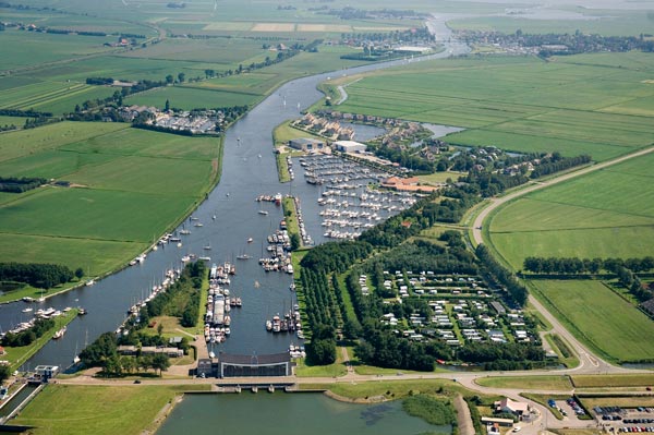 Op de voorgrond het elektrische J.L. Hooglandgemaal. Links de Johan Frisosluis in het gelijknamige kanaal. De grote jachthaven (Marina Stavoren binnen), de camping en het vakantiepark zijn van Skips Maritiem BV.