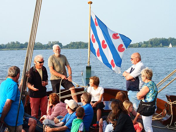 Vrijwillig schipper Sybren van der Meer, met zonnebril, stuurt de palingaak met toeristen over de Hegemer Mar terwijl hij verhaalt over het rijke palingverleden van Heeg, het Volendam van Friesland.