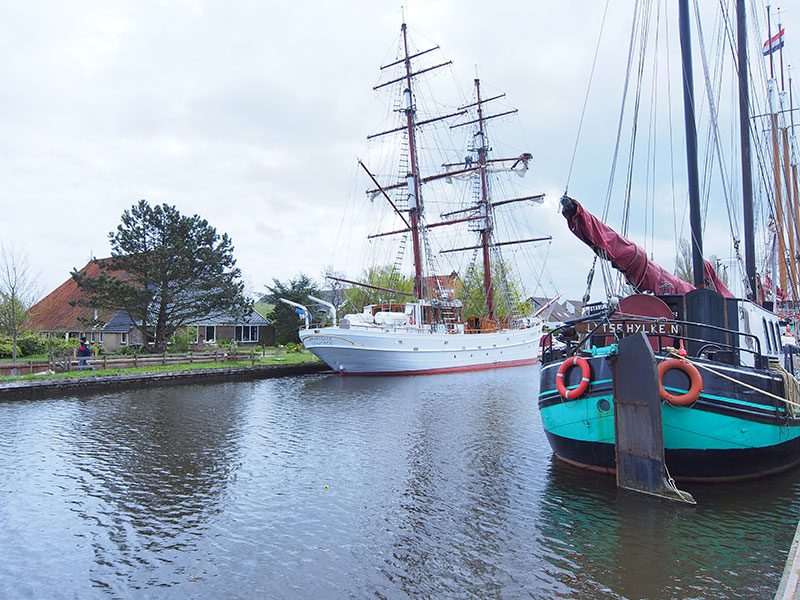 De Aphrodite voor de wal aan de Koeweg in Hanzestad Stavoren, voor de woonboerderij van Aent en Ellen Kingma. De tuigers zijn druk doende om het cruiseschip zeilklaar te maken.